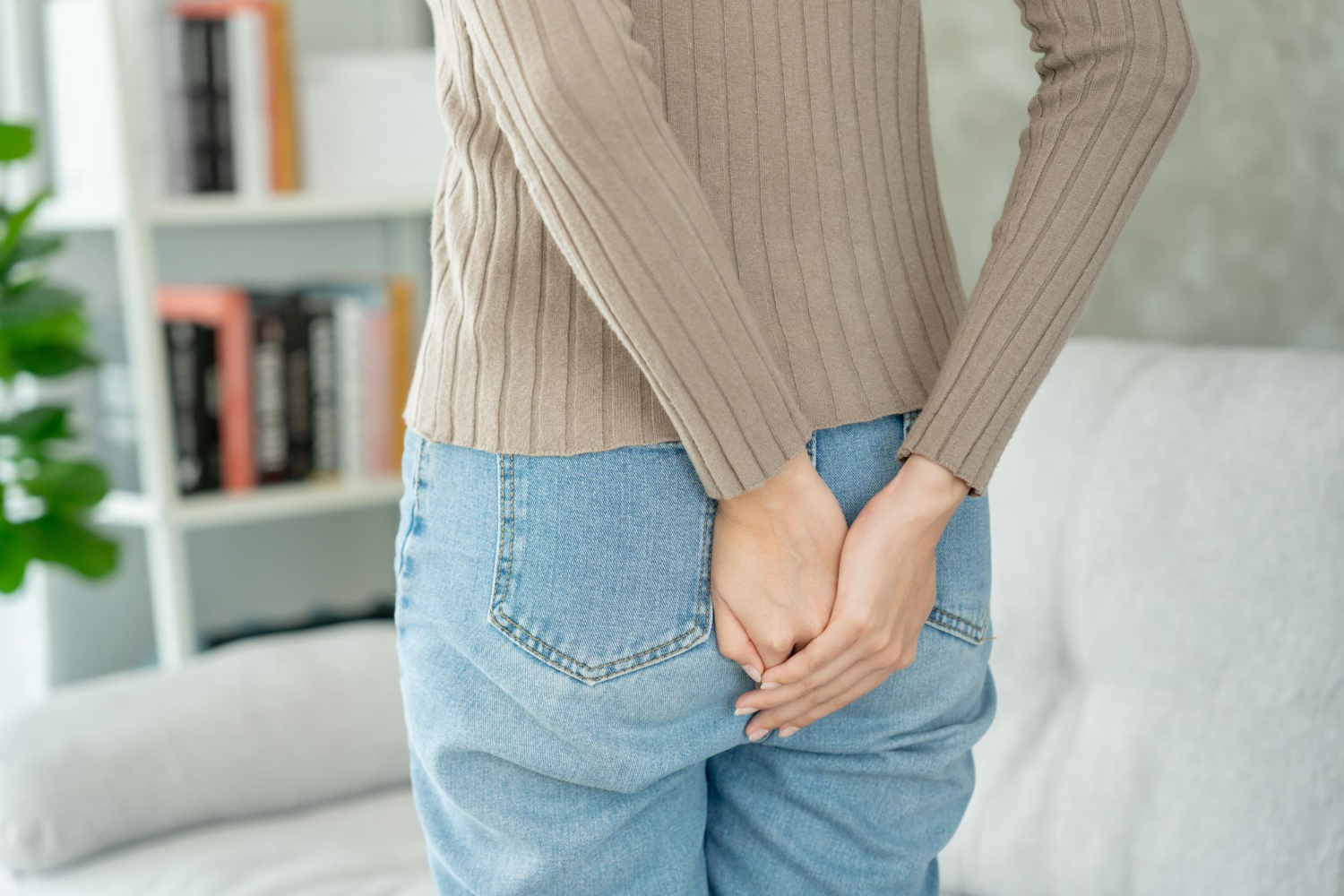 Kobieta w dżinsach trzyma obie ręce na bolącej pupie